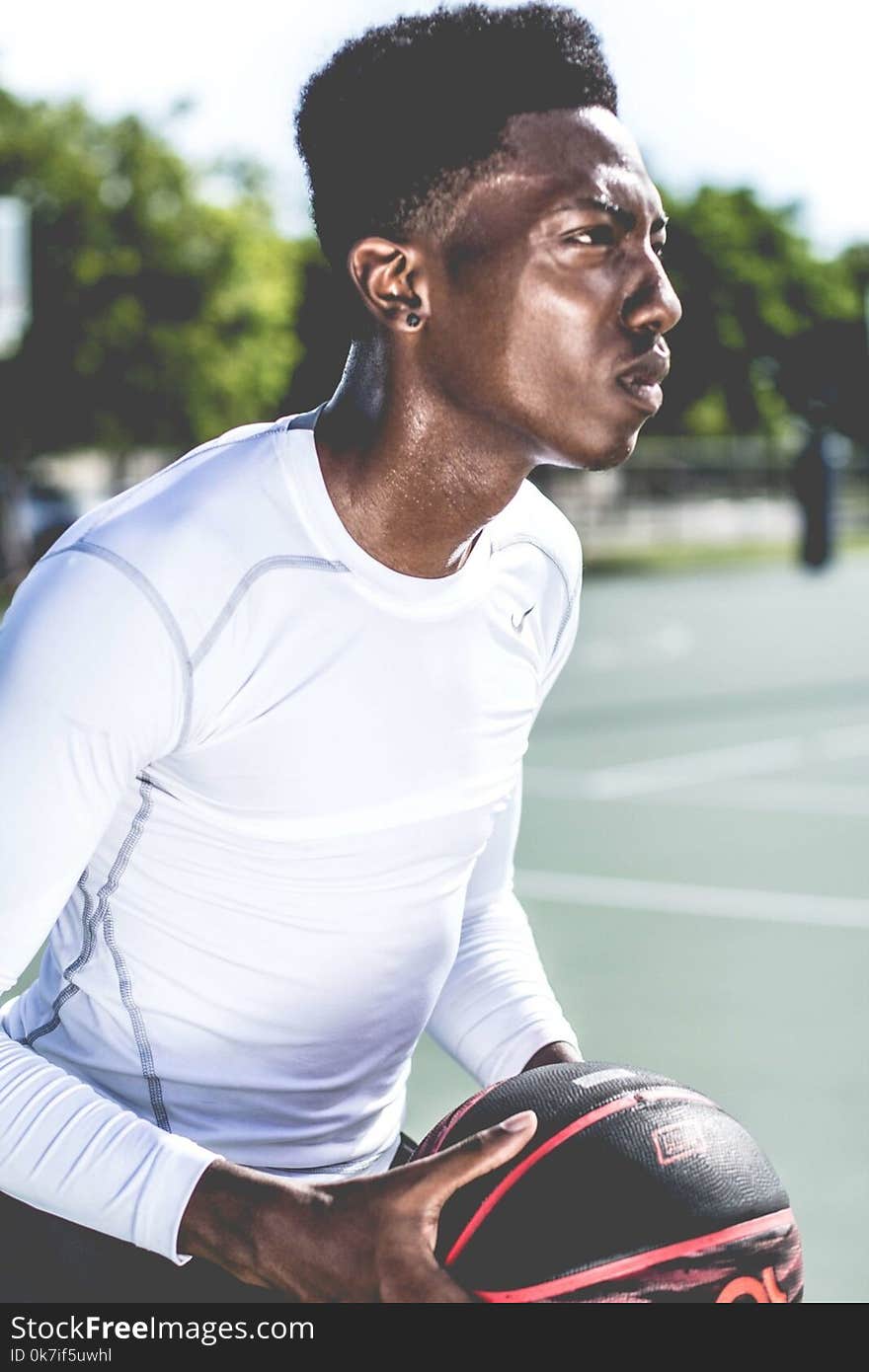 Man in White Crew-neck Long-sleeved Shirt Holding Black and Red Basketball