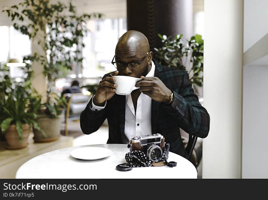 Man Sitting in Front of Round Table While Sipping from White Ceramic Mug