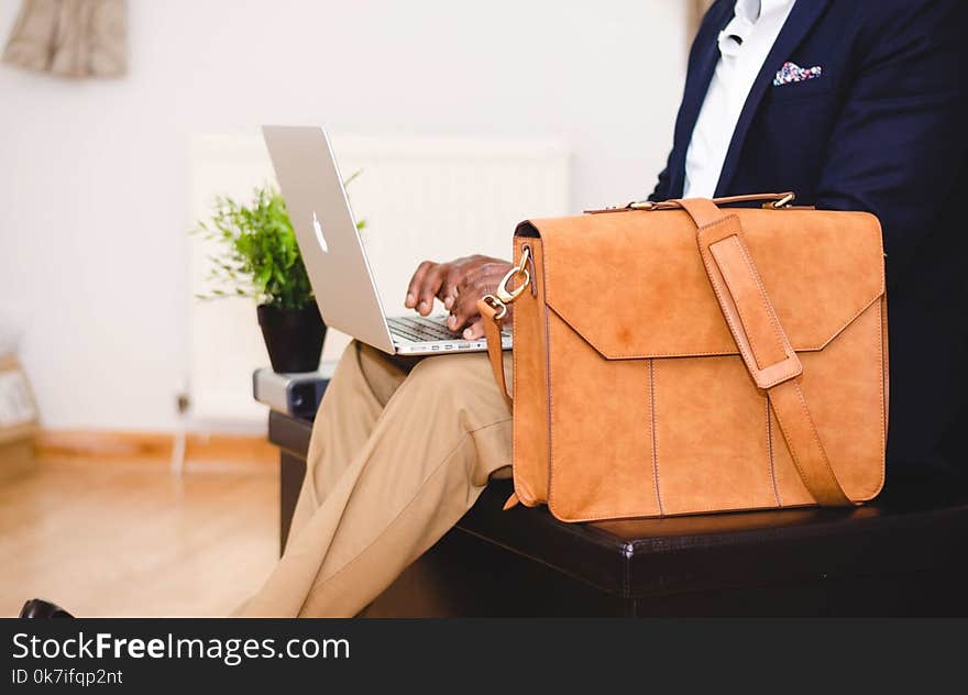 Person Wearing Blue Suit Beside Crossbody Bag and Using Macbook