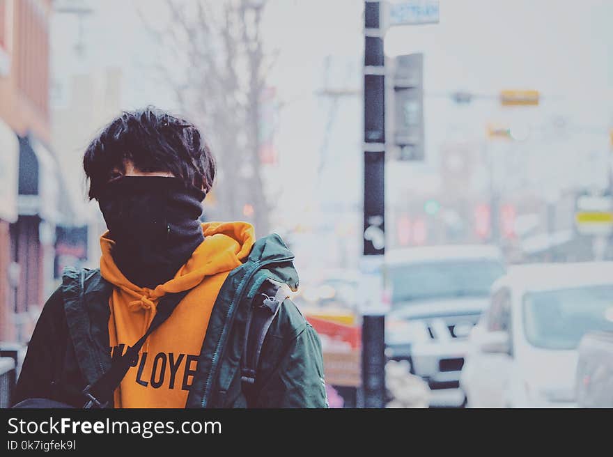 Man in Orange Pullover Hoodie and Green Jacket Covered With Black Mask