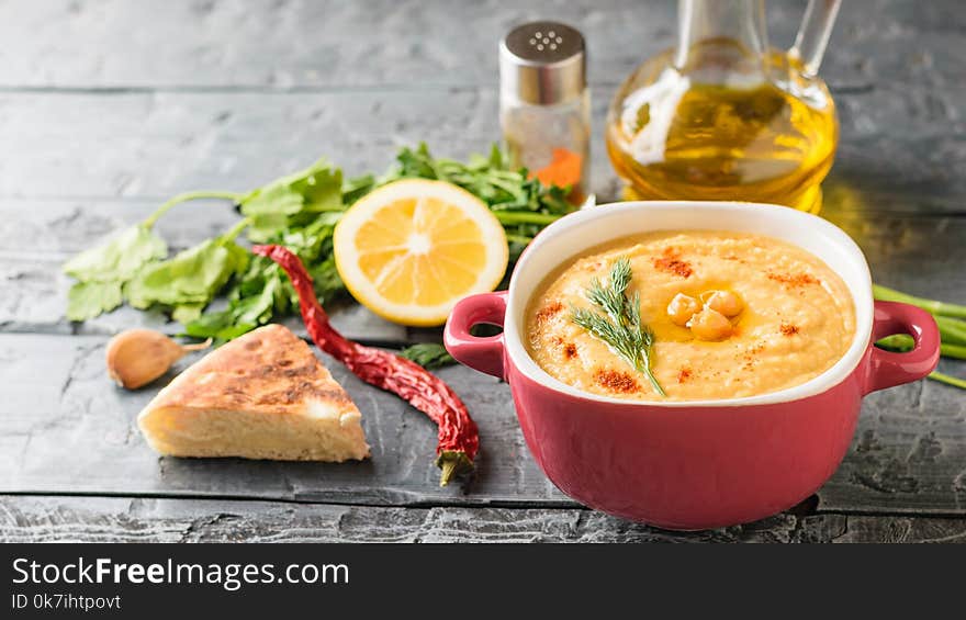 Freshly Made Hummus In A Purple Bowl, Jug With Olive Oil And Spices On A Wooden Table.