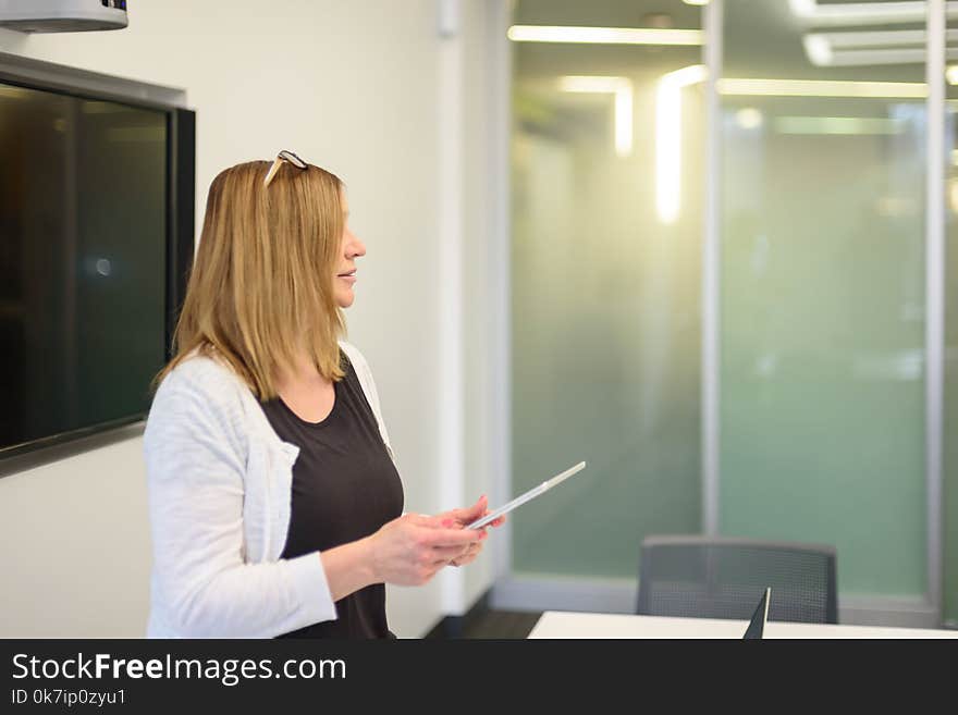 Businesswoman leading meeting holding tablet computer and standing by wall mounted tv. Businesswoman leading meeting holding tablet computer and standing by wall mounted tv