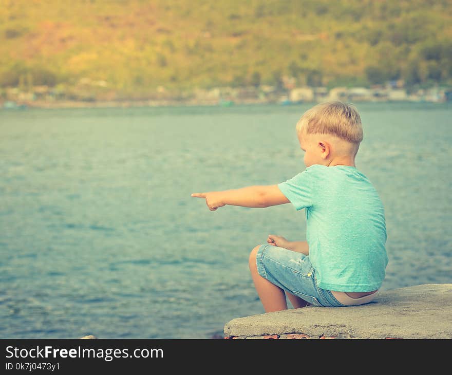 Cute caucasian boy pointing at seaside. Rear view. Leisure time