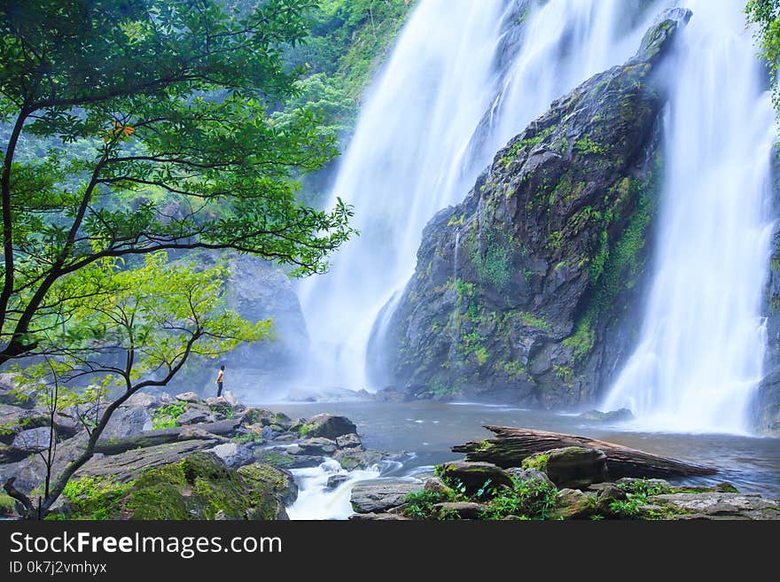 Young man relaxing on stone in front of flowing waterfall. Nature Therapy.