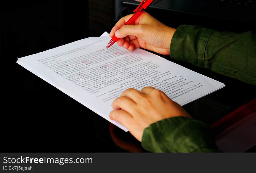 Hand holding red pen to correct proofreading paper on black table in office. Hand holding red pen to correct proofreading paper on black table in office