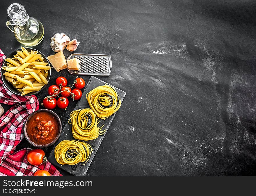 Composition of traditional Italian cuisine including cheese, variety of pasta, olive oil and tomatoes on grey culinary background. Top view, copyspace. Composition of traditional Italian cuisine including cheese, variety of pasta, olive oil and tomatoes on grey culinary background. Top view, copyspace