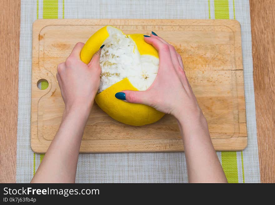 Girl cleans a pomelo on a wooden board