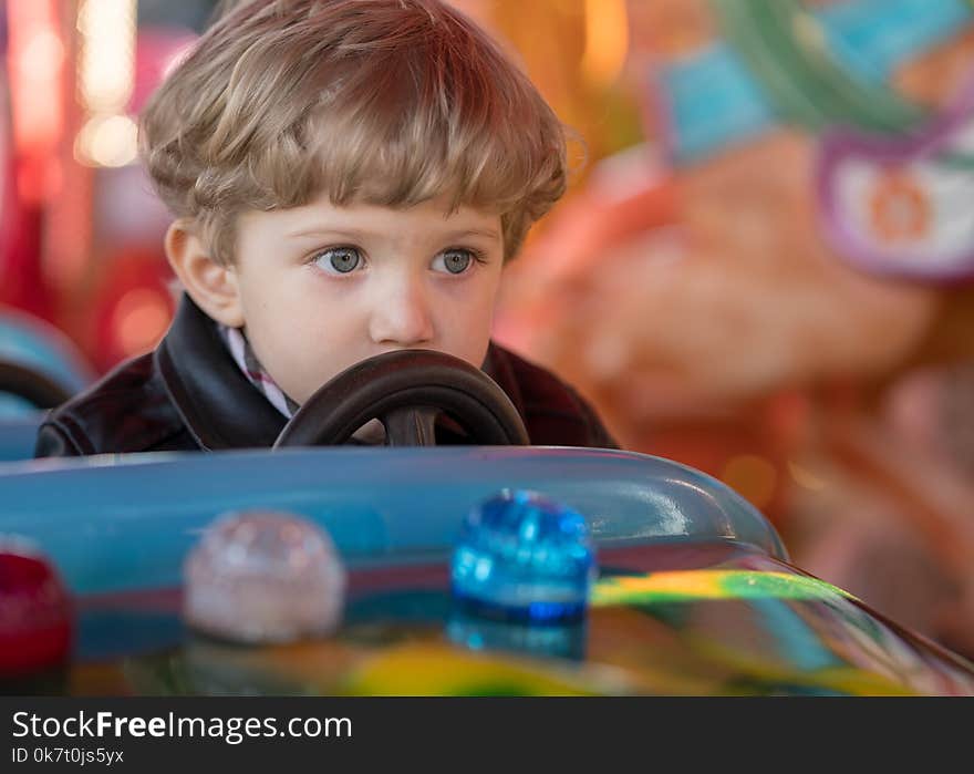 Kid boy drives a blue car at carousel