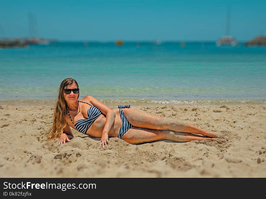 Woman in Blue and Black Bikini Lying on Beach Sand