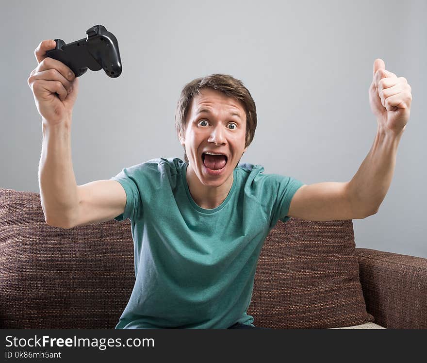 Handsome young man with smile sitting on sofa and holding controller and playing video games. Cheerful dude on sofa having fun with internet friends. Handsome young man with smile sitting on sofa and holding controller and playing video games. Cheerful dude on sofa having fun with internet friends