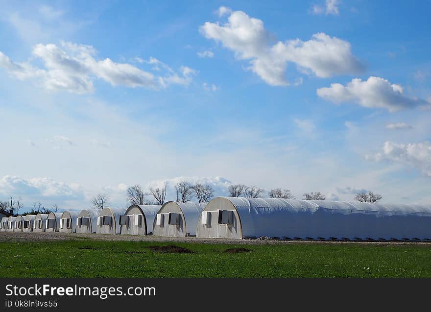 A Row Of Industrial White Greenhouses Under A Blue Sky With Clouds