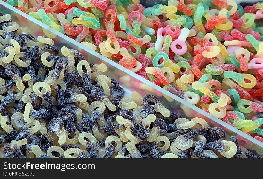 Gummy pacifier shaped candies in a shelf of a market. On the lower side they have two colors, in the upper side are multicolored