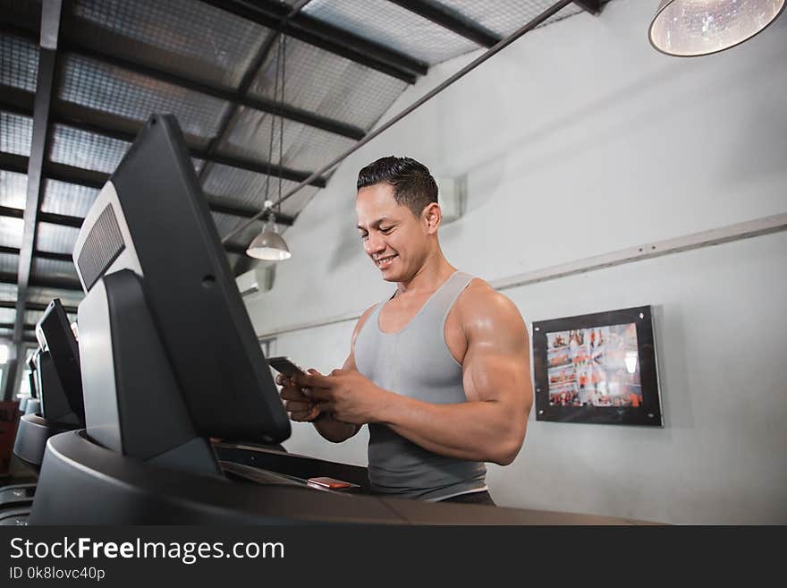 Muscular man on treadmill holding smartphone in the gym centre