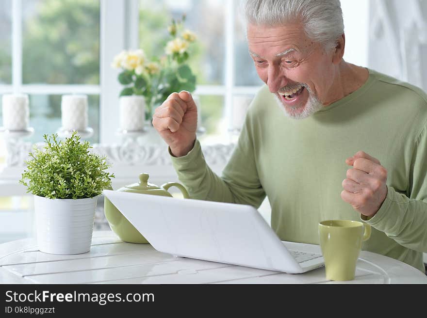 Emotional senior man using laptop at home