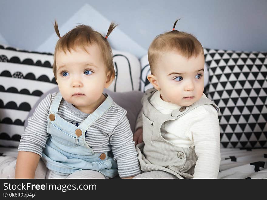 Two happy little sisters sitting on black and white sofa. Toddler, kid. Family with children at home. Two happy little sisters sitting on black and white sofa. Toddler, kid. Family with children at home.