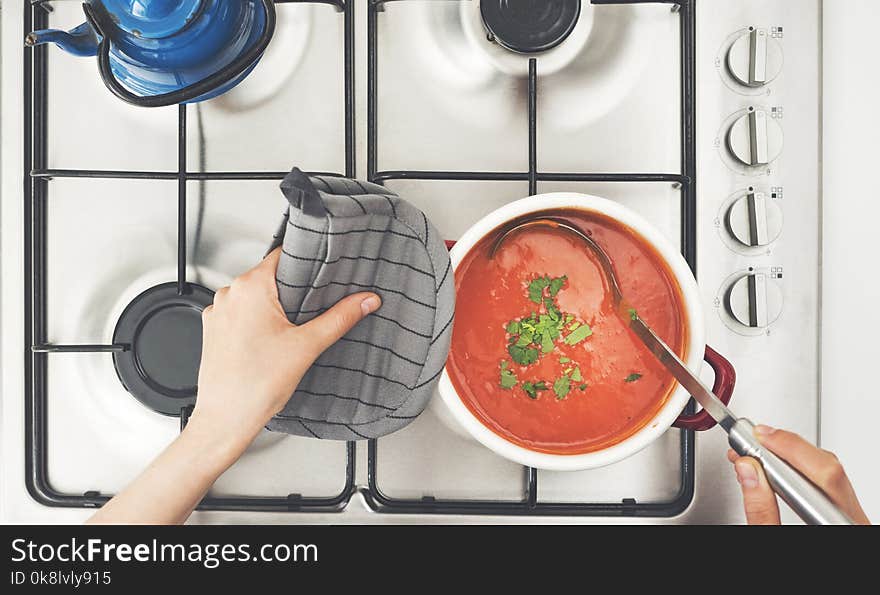 Woman cooking tomato soup on stove in kitchen