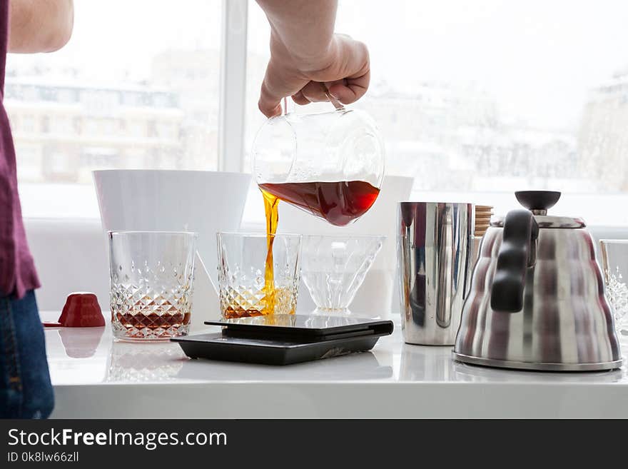 A man pours coffee for a sample from a decanter into faceted transparent glasses. A man pours coffee for a sample from a decanter into faceted transparent glasses.