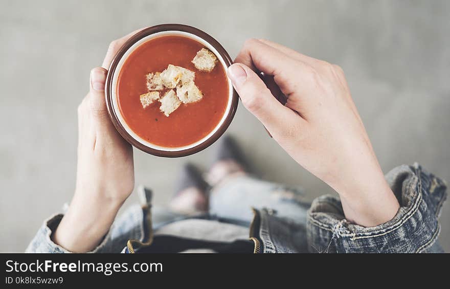 Woman holding tomato soup cup with croutons