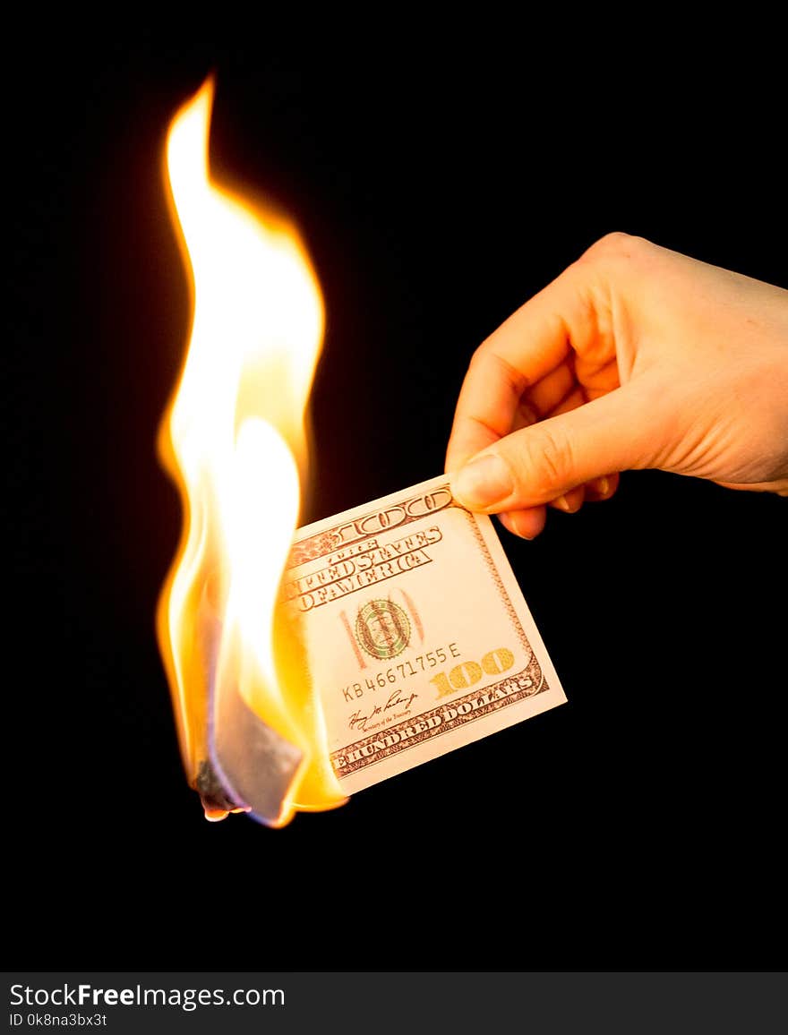 One hundred dollars burn in the hand on a black background .