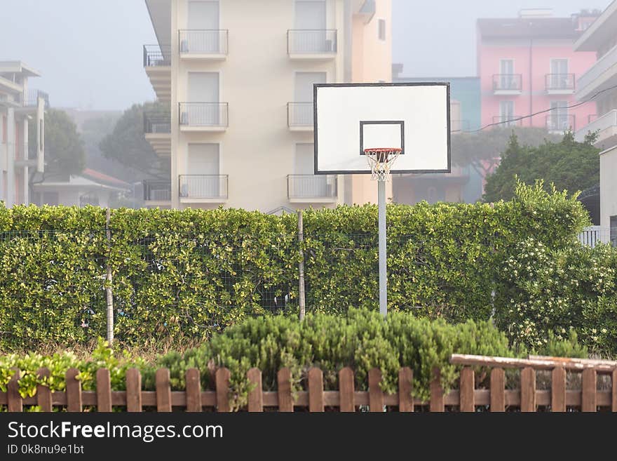 Basketball structure in an outdoor playground surrounded by trees in a park.