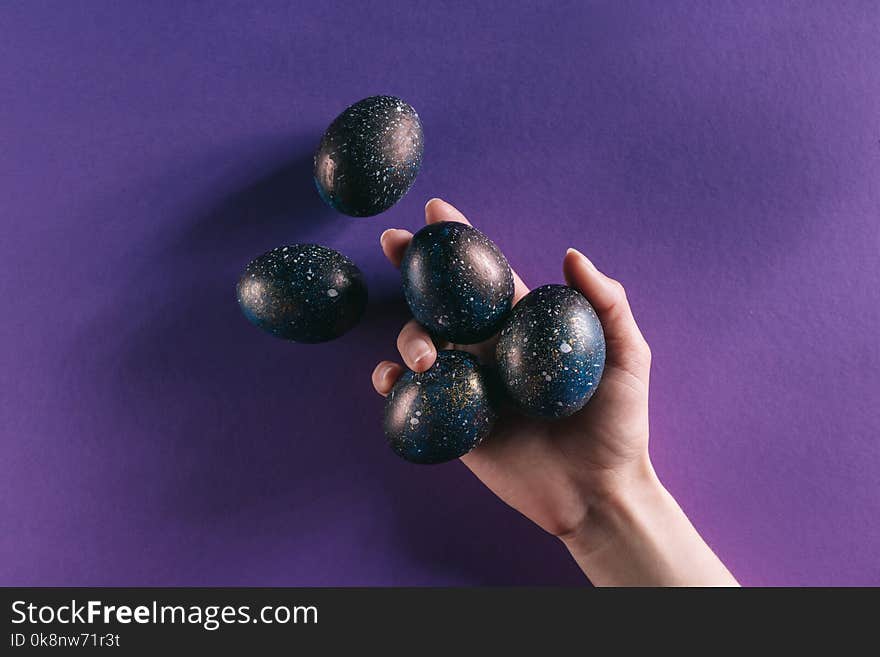 Cropped image of woman holding painted easter eggs above violet surface