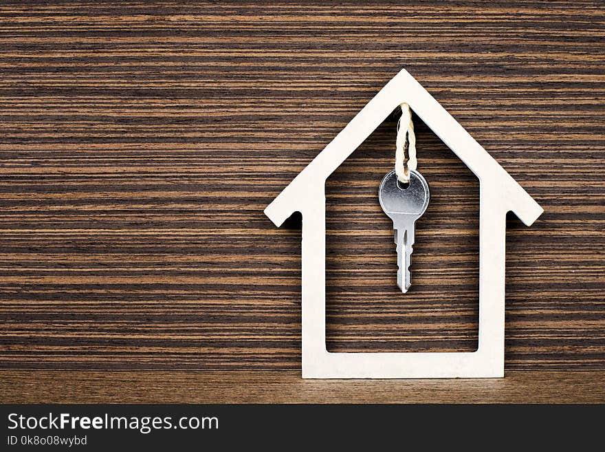 Silver key hanging inside white house on vintage wooden background. Concept for real estate, moving home or renting property. Silver key hanging inside white house on vintage wooden background. Concept for real estate, moving home or renting property.