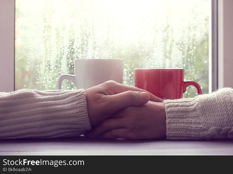 Two people hold each other hands, against a background of cups and a window with drops after a rain. Two people hold each other hands, against a background of cups and a window with drops after a rain