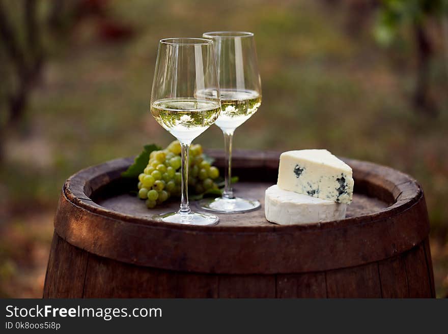 Pair of white wine glasses on wooden barrel with grapes