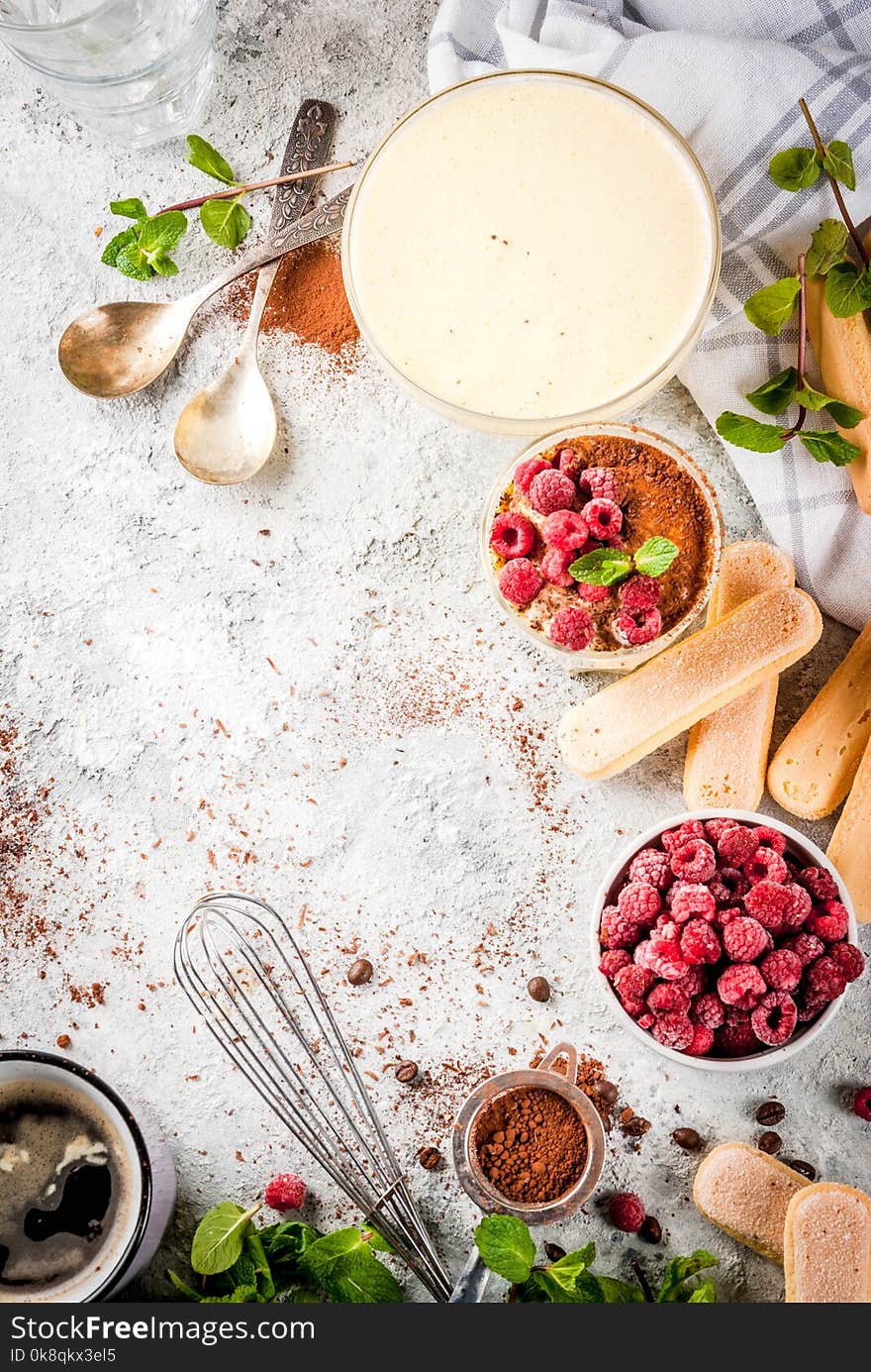 Cooking Italian food dessert Tiramisu, with all the necessary ingredients cocoa, coffee, mascarpone cheese, mint and raspberries, on grey stone background. Copy space top view. Cooking Italian food dessert Tiramisu, with all the necessary ingredients cocoa, coffee, mascarpone cheese, mint and raspberries, on grey stone background. Copy space top view