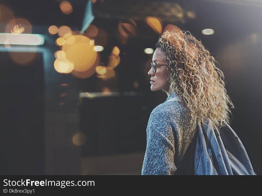 Pretty woman in stylish clothing wearing eye glasses traveling in the european night city. Bokeh and flares effect on blurred background