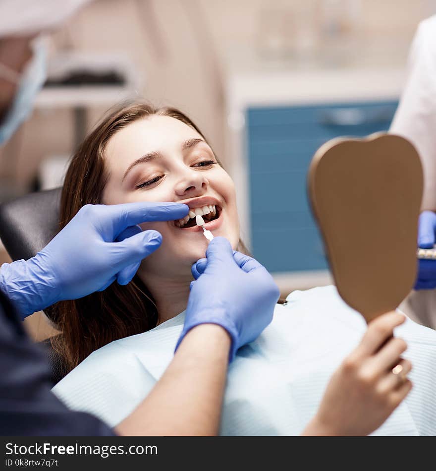 Male dentist comparing patient`s teeth shade with samples for bleaching treatment.