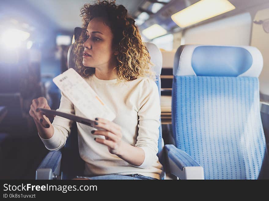 Enjoying business travel concept. Young beautiful brunette tourist girl travelling on the train sitting near the window using smartphone,holding ticket hands