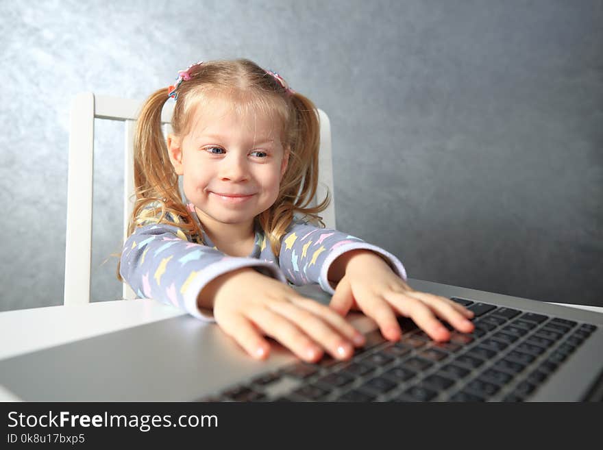 Smiling little girl studying computer. Girl using laptop keyboard.