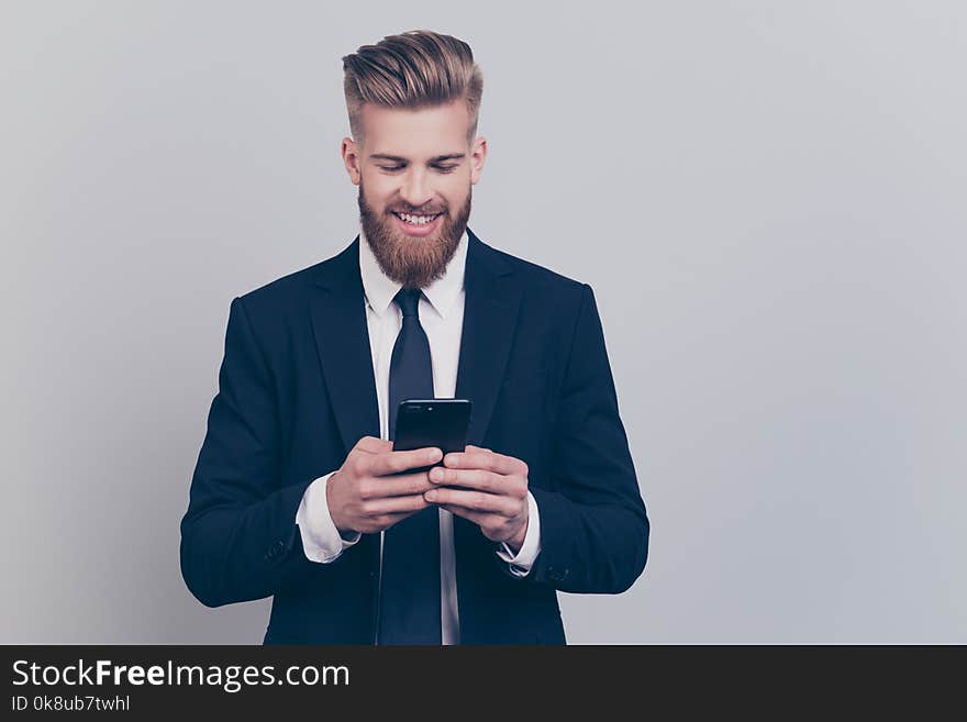 Portrait of handsome with stylish hairdo cheerful funny excited financier using smartphone playing online games receiving getting writing sms updating his digital gadget isolated on gray background. Handsome guy.