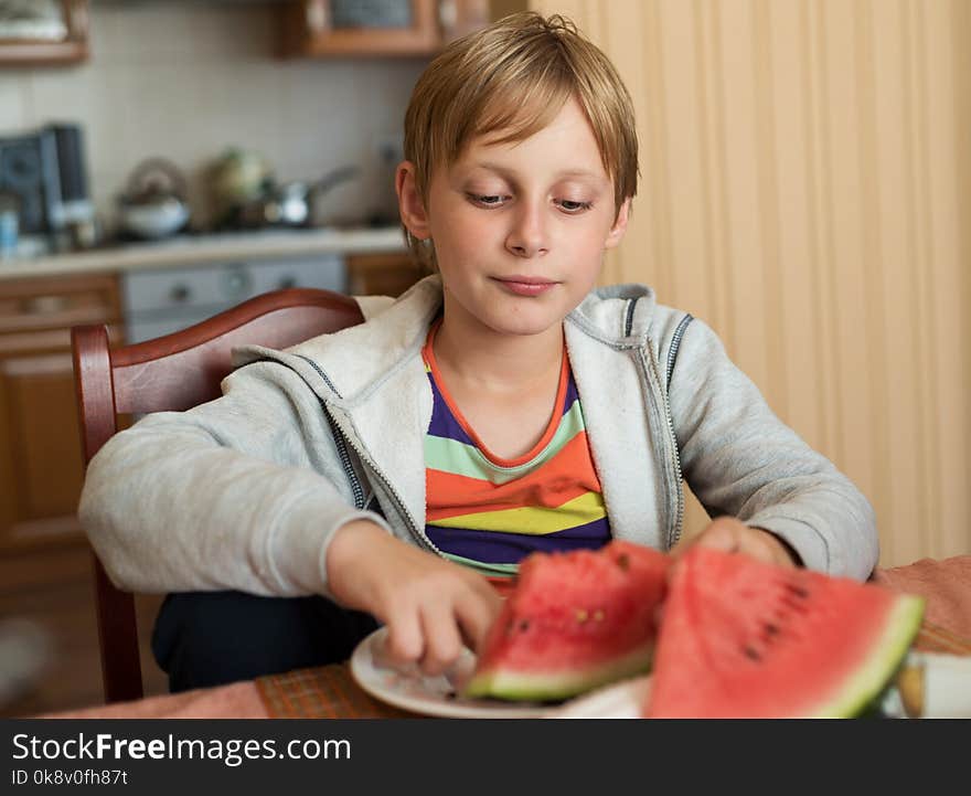 Boy sitting at home at the table and eating watermelon