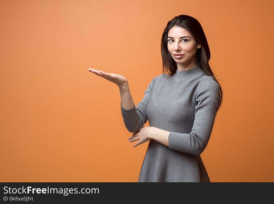 Portrait of a young beautiful business woman in neutral dress holding out empty hand and looking into camera