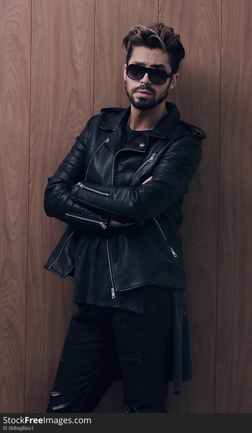 Image of a fashion side man stands with crossed hands on a wooden background. Image of a fashion side man stands with crossed hands on a wooden background