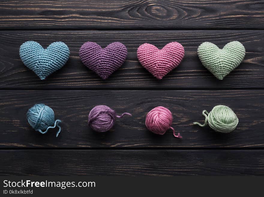 Colorful handicraft crocheted hearts & skeins of yarn on old gray wooden table. Retro color palette. Making a love message. Colorful handicraft crocheted hearts & skeins of yarn on old gray wooden table. Retro color palette. Making a love message