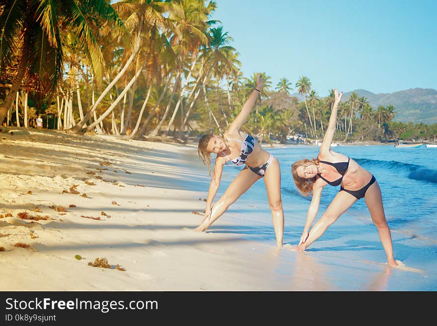 Two girls doing physical exercises on a tropical beach