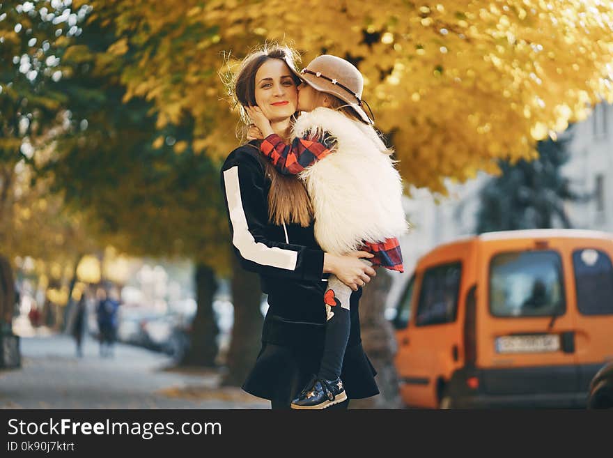 Young beautiful long-haired mother in black dress walks with a little stylish daughter in the autumn city. Young beautiful long-haired mother in black dress walks with a little stylish daughter in the autumn city