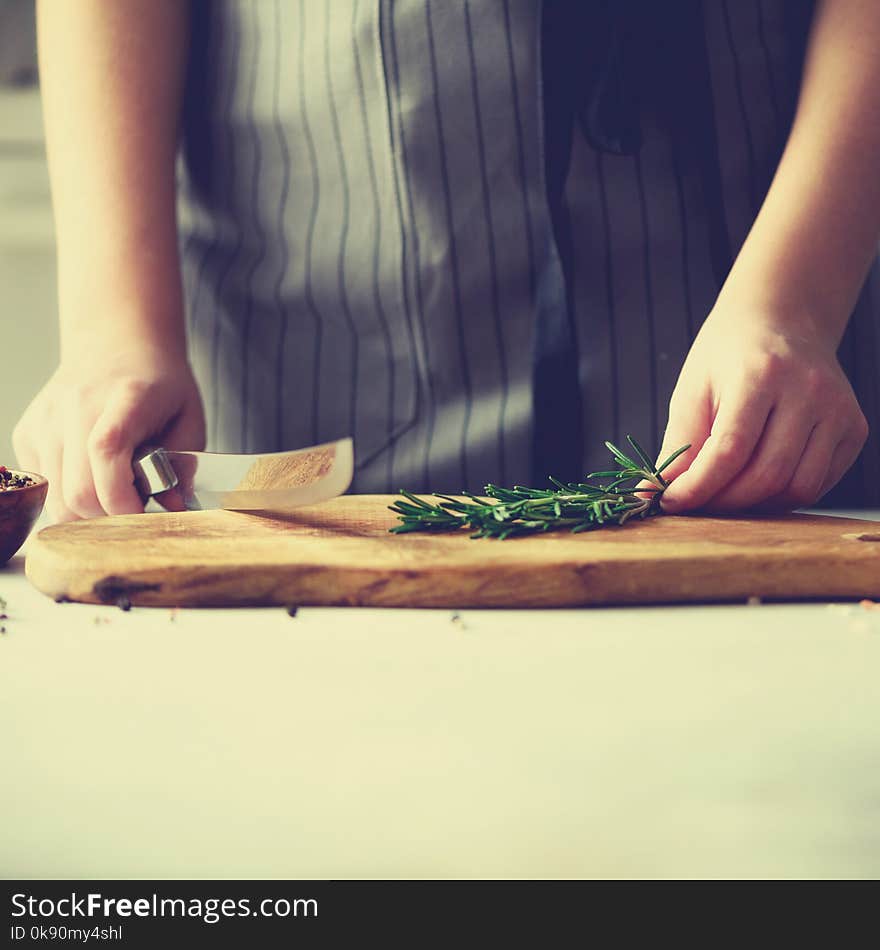 Woman hands cutting fresh green rosemary on wood chopping board in white kitchen, interior. Copy space. Homemade food conceplt, healthy recipe.