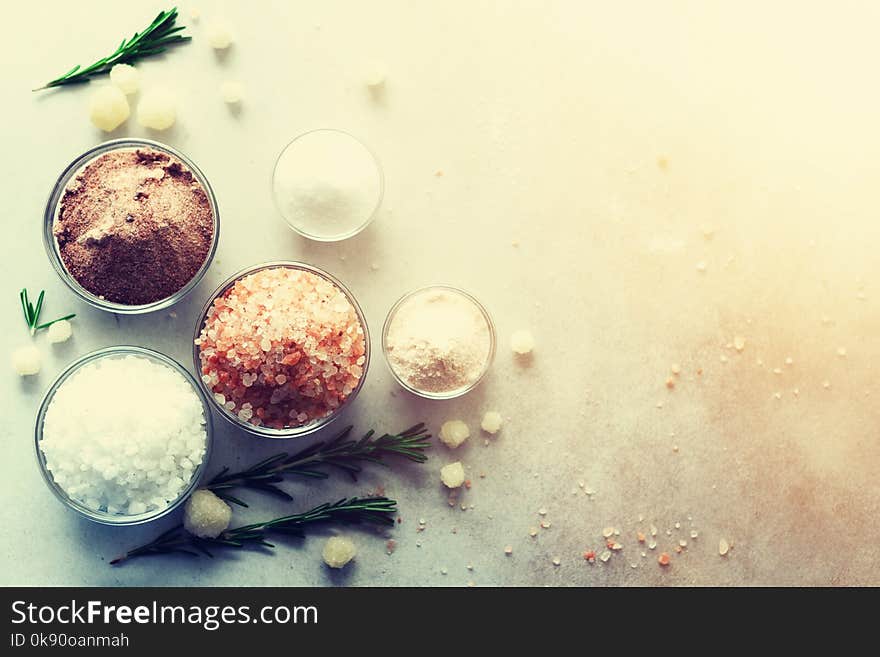 Mix of different salt types on grey concrete background. Sea salts, black and pink Himalayan salt crystals, powder, rosemary. Salt crystal balls from Dead sea. Copy space. Top view