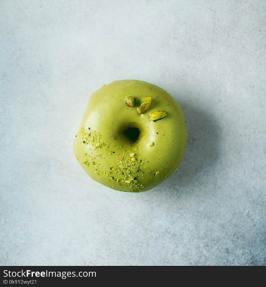 Sweet doughnut with green glaze and pistachio on grey background. Tasty donut on pastel concrete texture, copy space, top view.