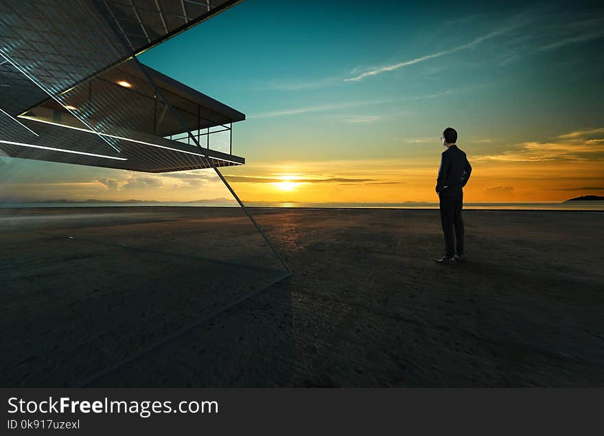 Businessman looks at sunrise thoughtfully with steel and glass facade modern building background .