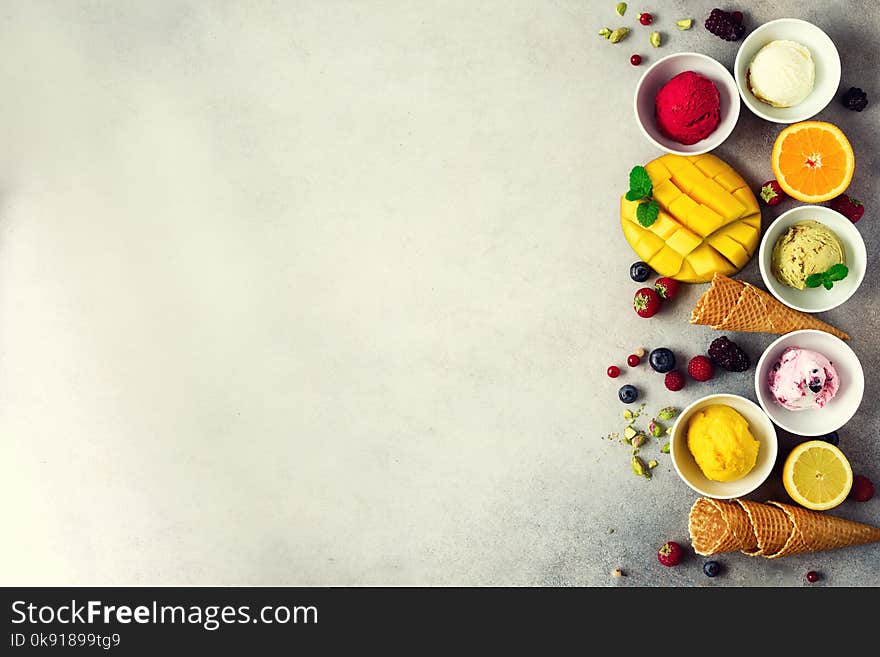 Ice Cream Balls In Bowls, Waffle Cones, Berries, Orange, Mango, Pistachio On Grey Concrete Background. Colorful