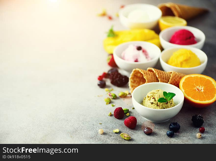 Ice cream balls in bowls, waffle cones, berries, orange, mango, pistachio on grey concrete background. Colorful collection, flat lay, summer concept.