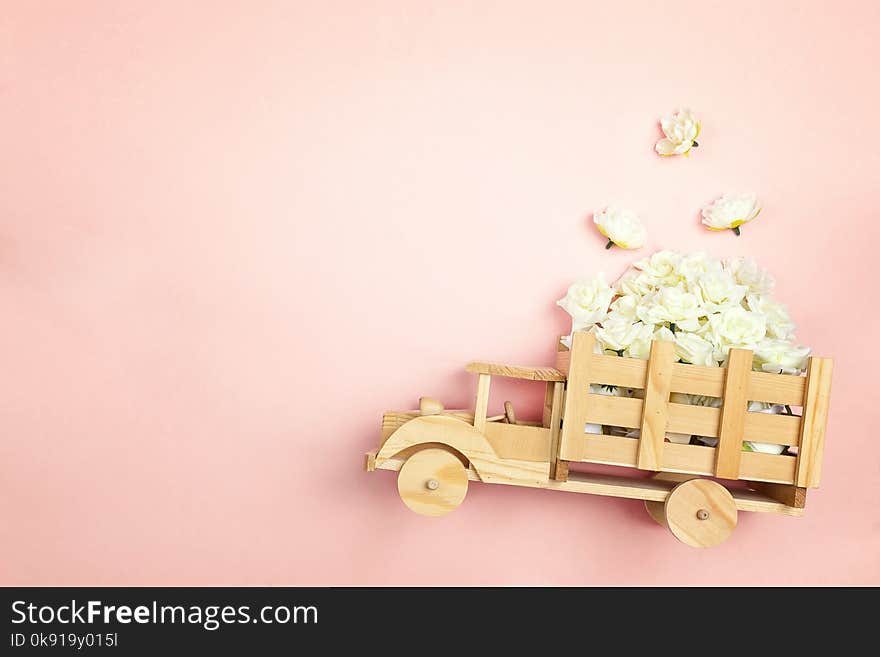 Wooden toy truck with white roses flowers in the back on pink background. Space for text. Festive greeting concept