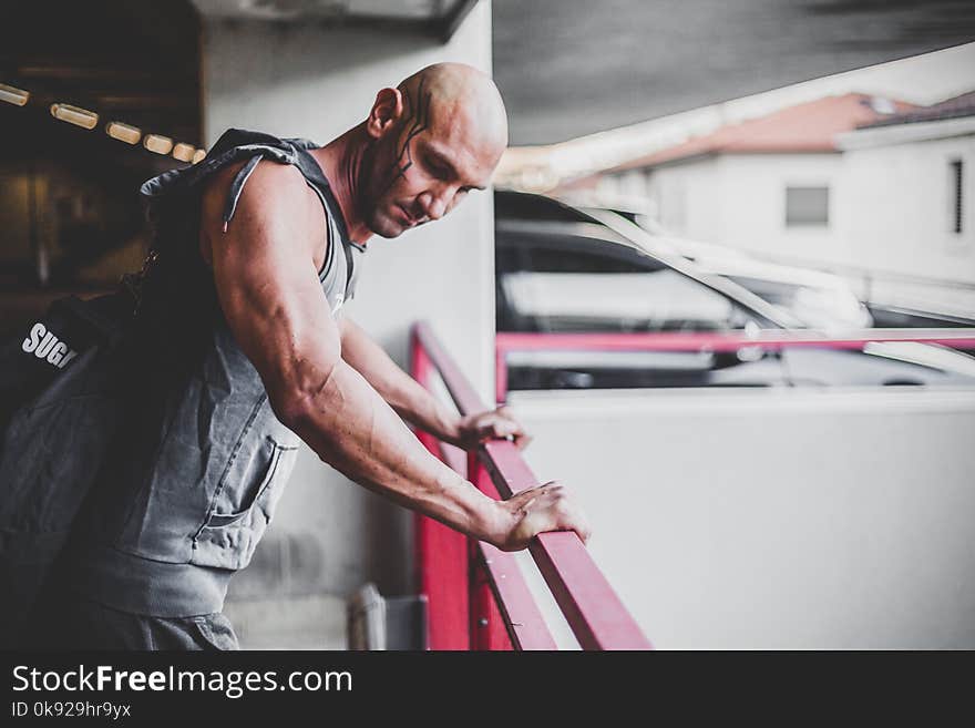 Man Wearing Grey Hooded Vest Holding Red Hand Rail on Parking Lot at Daytime