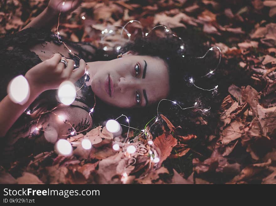 Woman Lying on Dried Leaves Holding String Lights