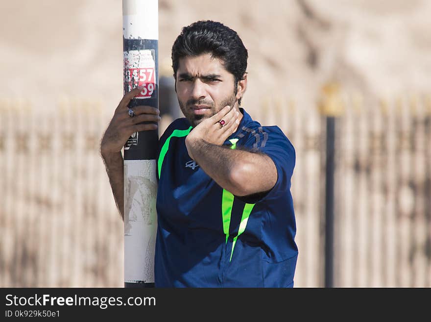 Man in Blue and Green T-shirt Holding on White Post